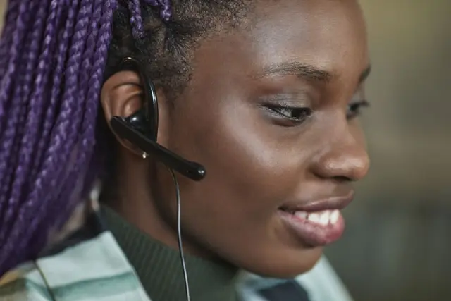 A support agent wearing a headset, smiling while she talks to a customer